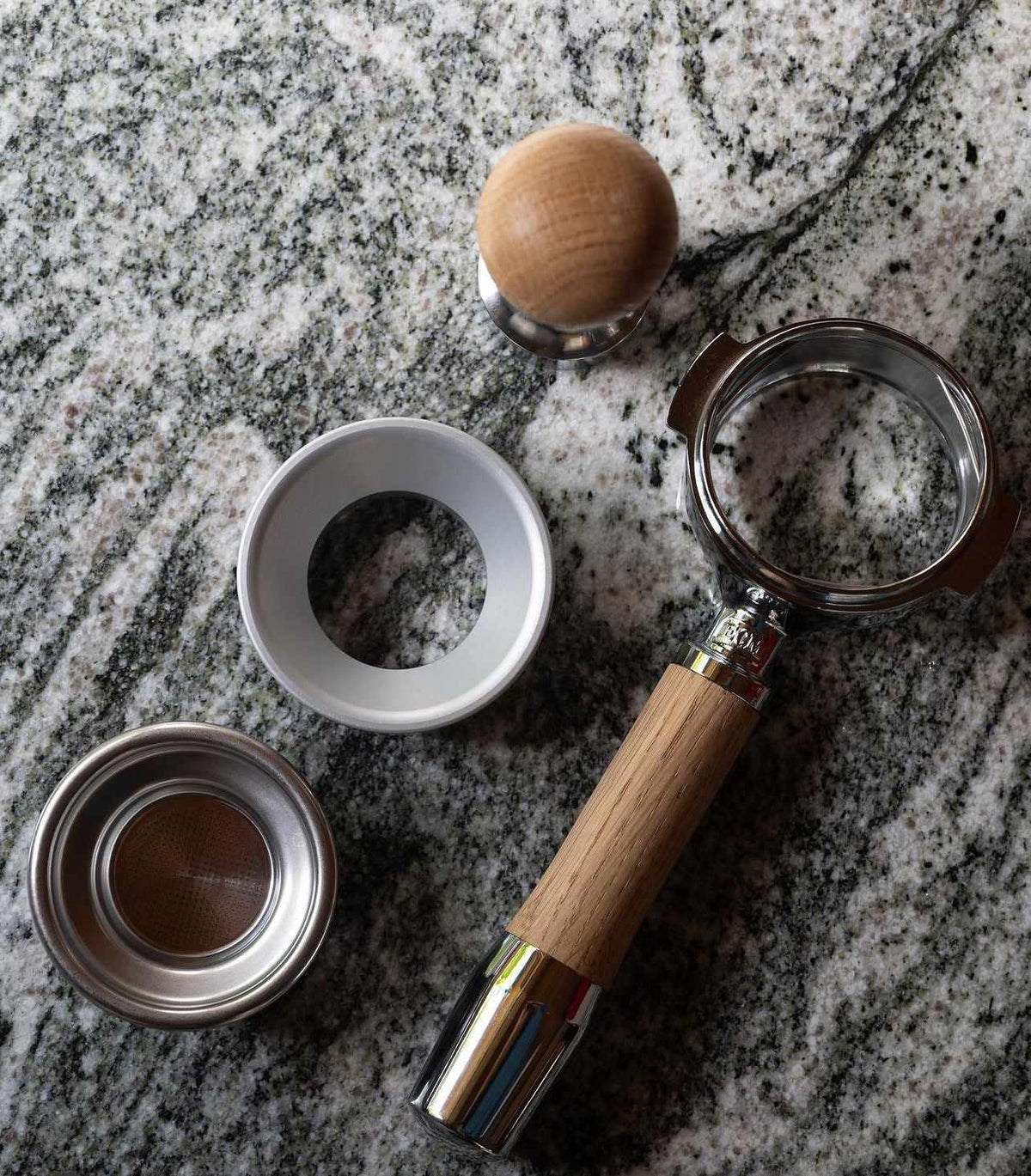 Espressotillbehör med tamper, tratt, portafilter och filterkorg på marmorbord.