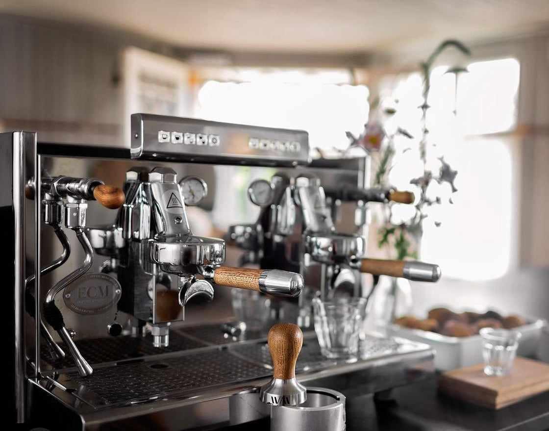 Espressomaskin med trähandtag i ett ljust kök med suddig bakgrund och kaffetillbehör runtomkring.