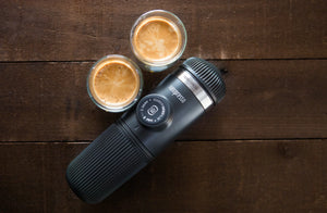 Pārnēsājama espresso kafijas automāts ar divām espresso tasītēm uz koka virsmas, no pārnēsājamām kafijas pagatavošanas ierīcēm un baristas aprīkojuma